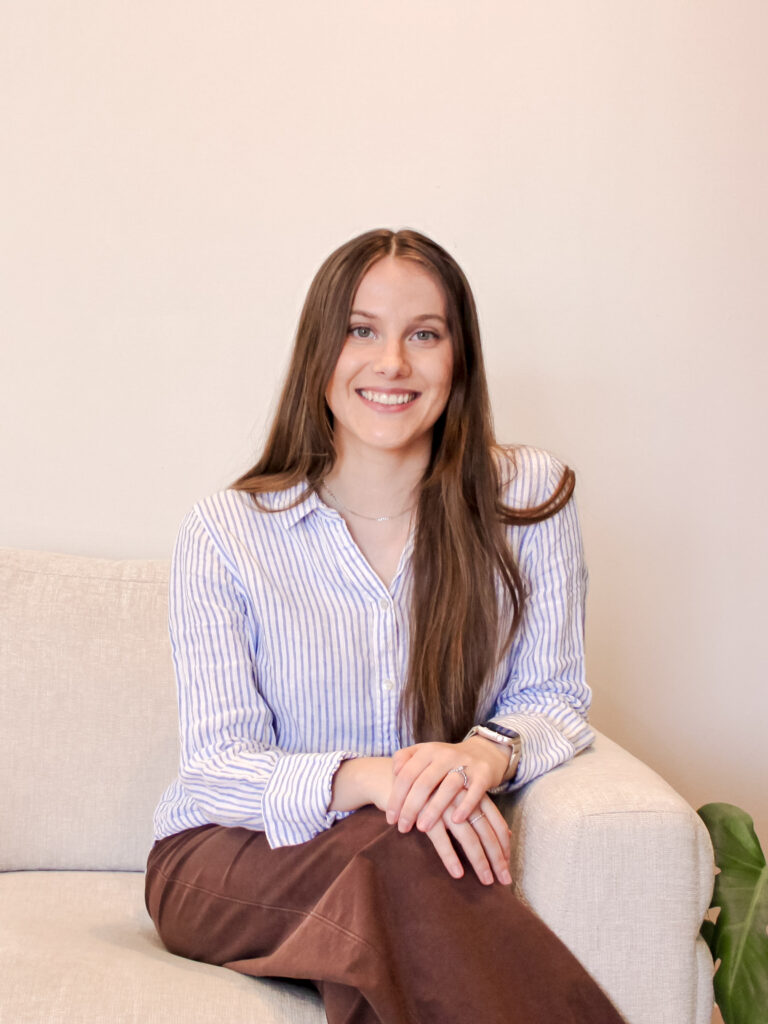 Shawna Tiles, Registered Psychotherapist (Qualifying), sitting on a comfortable couch and smiling, reflecting a warm and supportive therapeutic environment providing virtual therapy.